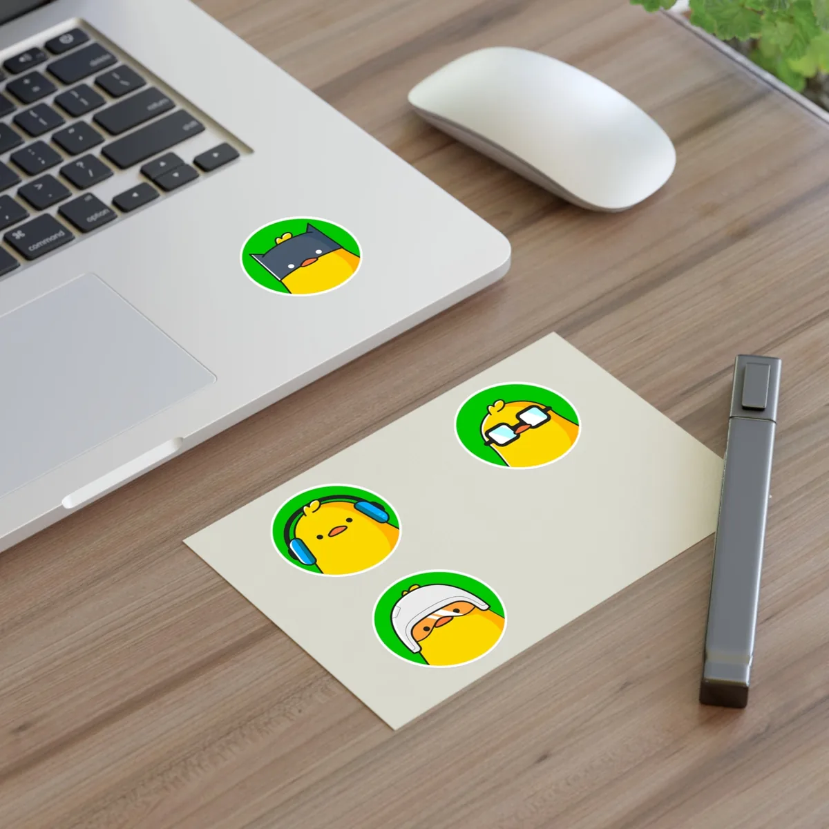 Round duck stickers on a laptop and a sticker sheet on a desk